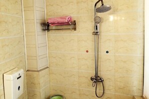Une douche avec un pommeau de douche amovible, un porte-serviettes avec une serviette rose et un distributeur de savon.