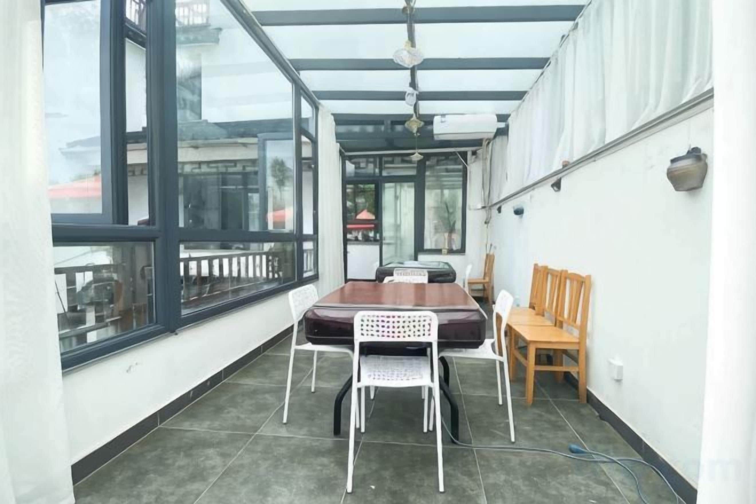 A covered balcony with a table and chairs, a wooden chair, and a view of the city.