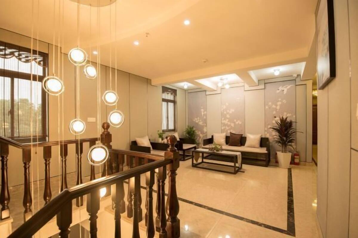A spacious lobby with a wooden staircase, a seating area with sofas, and a large window providing natural light.