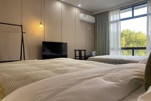 Une chambre d’hôtel avec deux lits, une télévision, un appareil de climatisation, une fenêtre avec des rideaux et un luminaire suspendu.