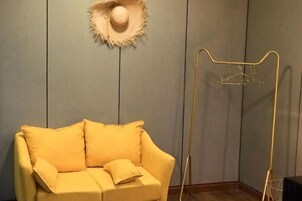 Una habitación con un sofá amarillo, un sombrero en la pared y un tendedero metálico.