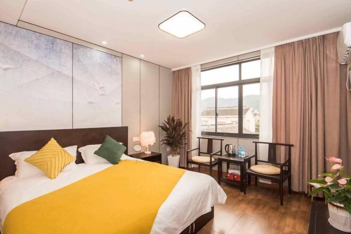 A hotel room with a bed, a small table with chairs, a window with curtains, and a plant.