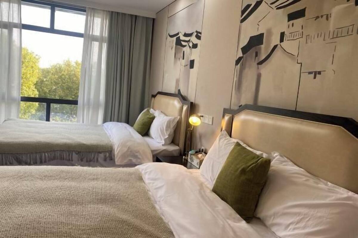 A hotel room with two beds, a large window, and a cityscape mural on the wall.
