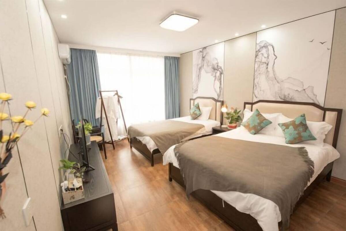 A hotel room with two beds, a desk with a computer, a wardrobe, and a large window with curtains.