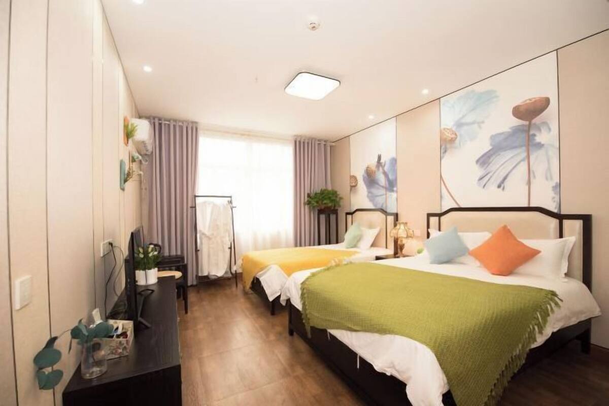 A hotel room with two beds, a desk, a chair, a TV, and a window with curtains.