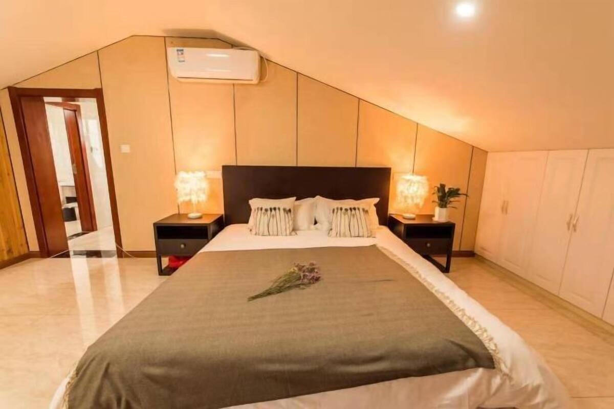 A bedroom with a sloped ceiling, a bed with a dark headboard, bedside lamps, a bedside table, and a wardrobe.
