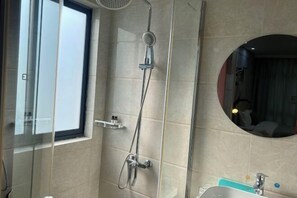 Une salle de bain moderne avec une douche à l’italienne en verre, un miroir rond et une fenêtre bien visible.