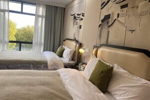 Habitación de hotel con dos camas, un ventanal grande con cortinas y una pared con arte abstracto.