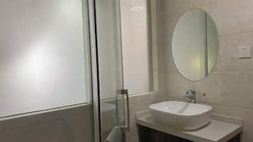 Un baño moderno con cabina de ducha de vidrio, un lavamanos blanco y un espejo grande en la pared.