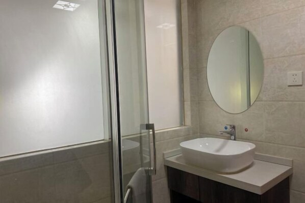 Une salle de bain moderne avec une douche à parois de verre, un lavabo blanc et un grand miroir au mur.