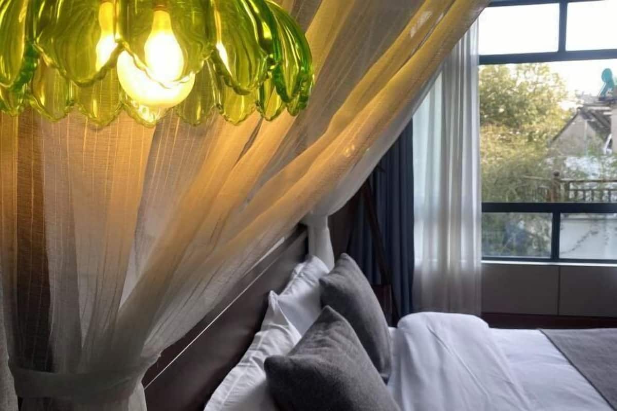 A room with a bed, sheer curtains, and a green light fixture.