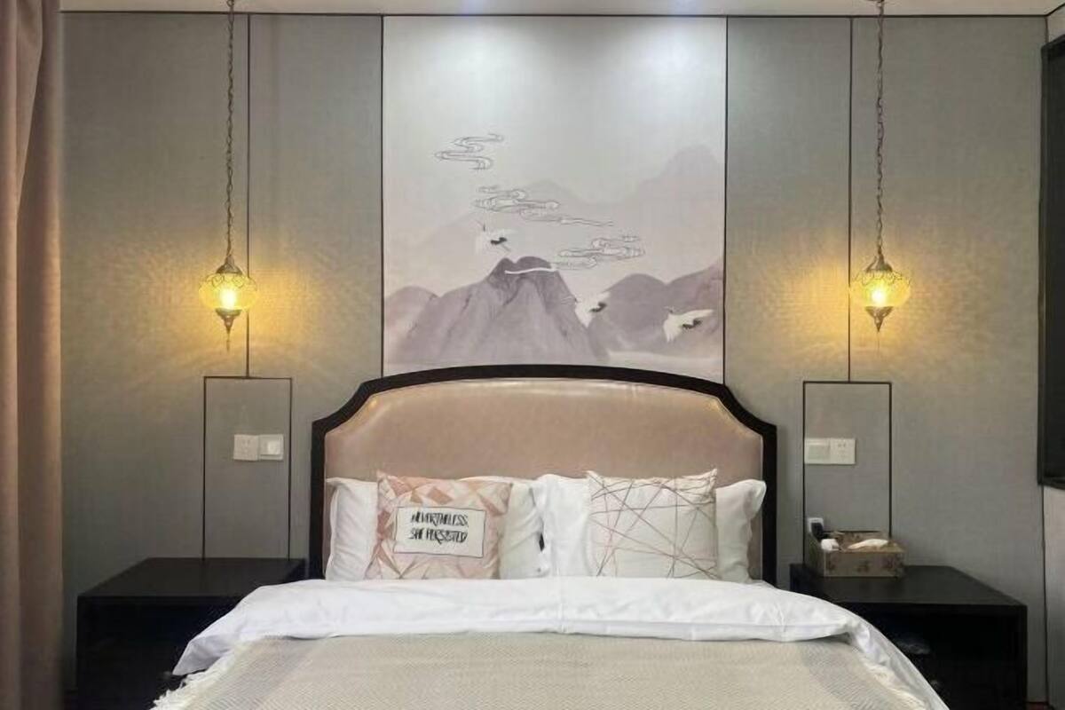 A bedroom with a bed, two bedside tables, a wall-mounted artwork, and two wall-mounted lamps.
