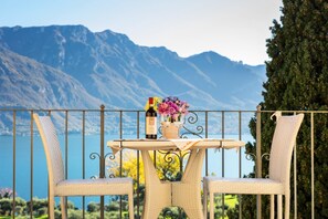 A balcony with wicker chairs, a table with a bottle and glasses, and a view of mountains and a lake. - Ca Maria Acero by Wonderful Italy (Bellagio)