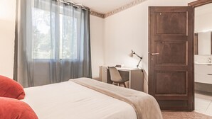 Een hotelkamer met een bed, een bureau, een stoel, een lamp en een houten deur.