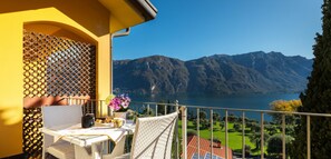 A balcony with a table set for breakfast, overlooking a lake and mountains.