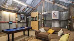 Un cuarto acogedor con mesa de billar, un sofá marrón con cojines, un dardo y un proyector en la pared.