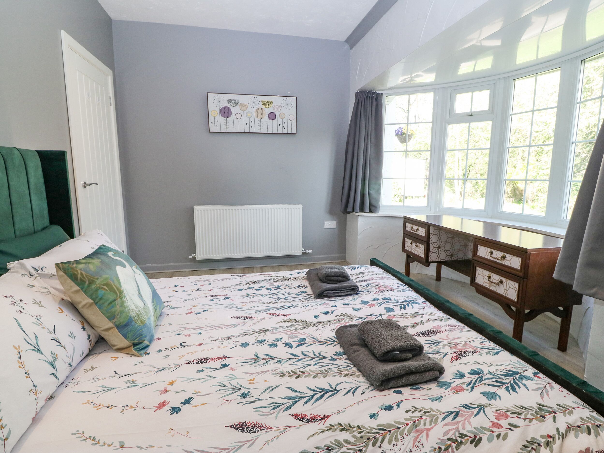 Une chambre à coucher comprenant un lit, un radiateur, une fenêtre avec des rideaux, une table de chevet et une œuvre d’art murale.