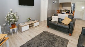 Una sala moderna con un televisor de pantalla plana, un sofá, una mesa de centro y una mesita auxiliar con una planta.