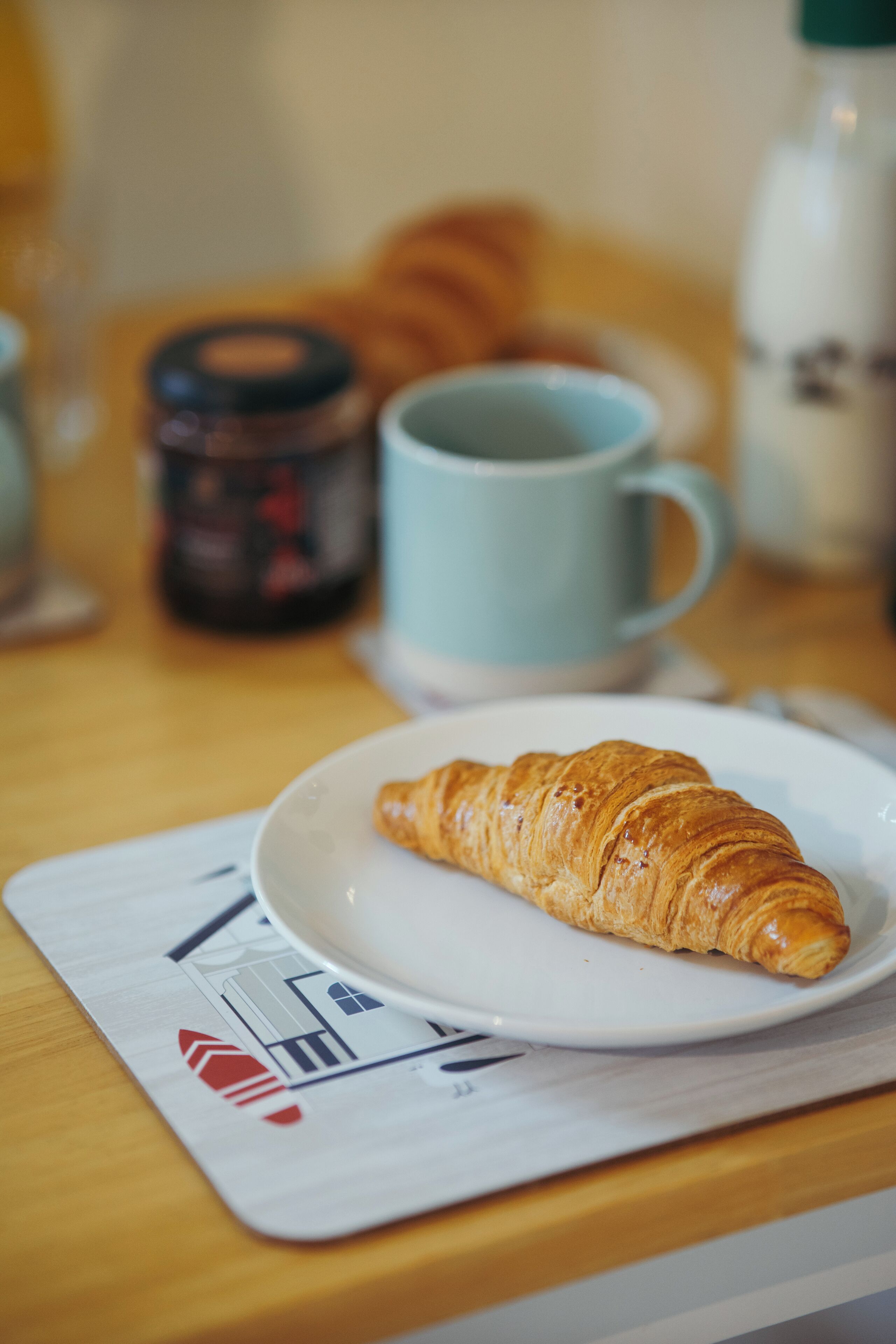 A croissant on a white plate on a wooden table.