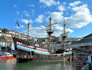 Un'imbarcazione a vela storica ormeggiata in un porto, con edifici sullo sfondo.