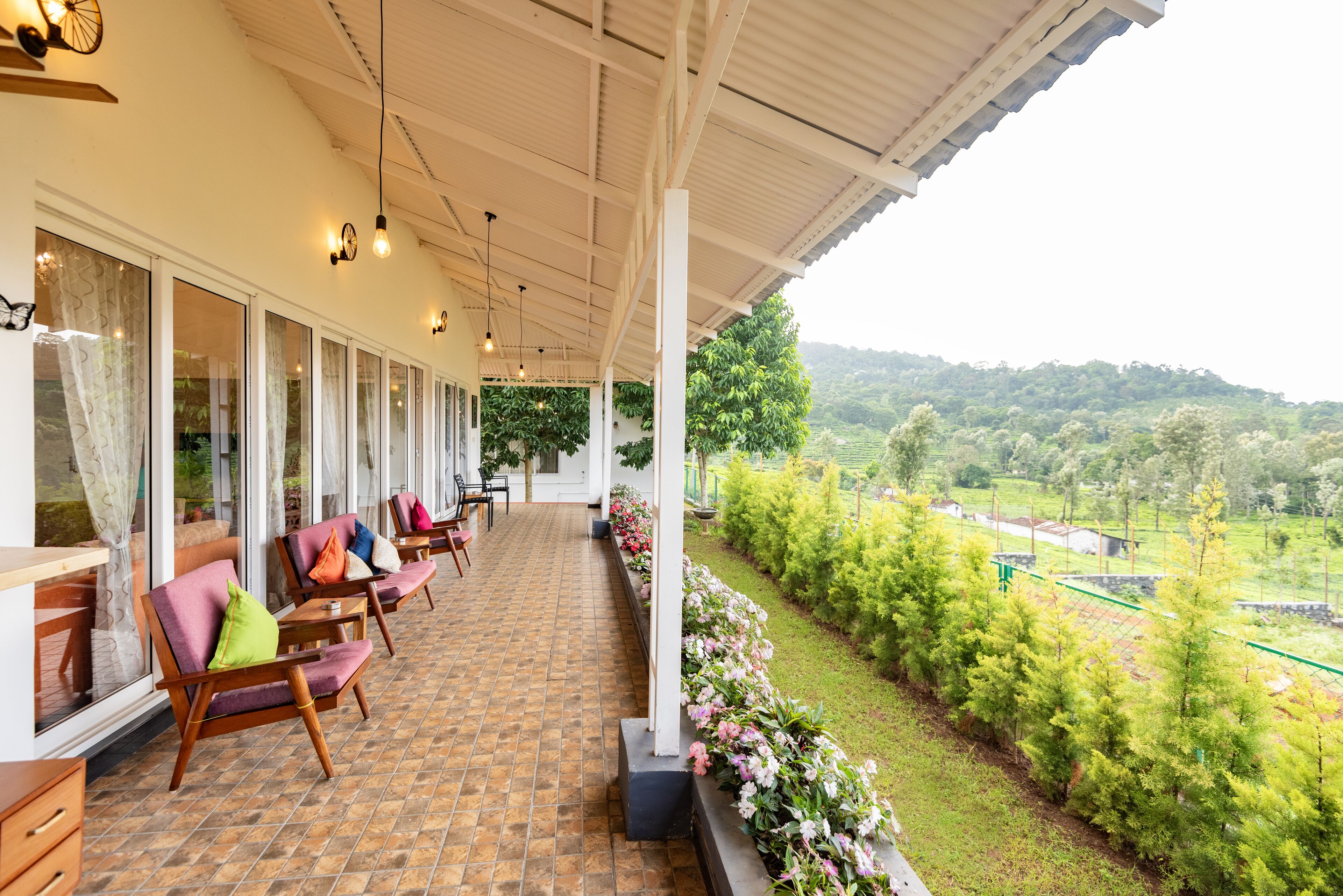 A covered outdoor seating area with chairs and tables, a tiled floor, and a view of a lush green landscape.