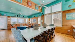 A beach-themed room with a wooden ceiling, a ceiling fan, a dining table with chairs, and a sofa. - Located in the sought-after gated Village Walk community is a charming tropical (Port Aransas)
