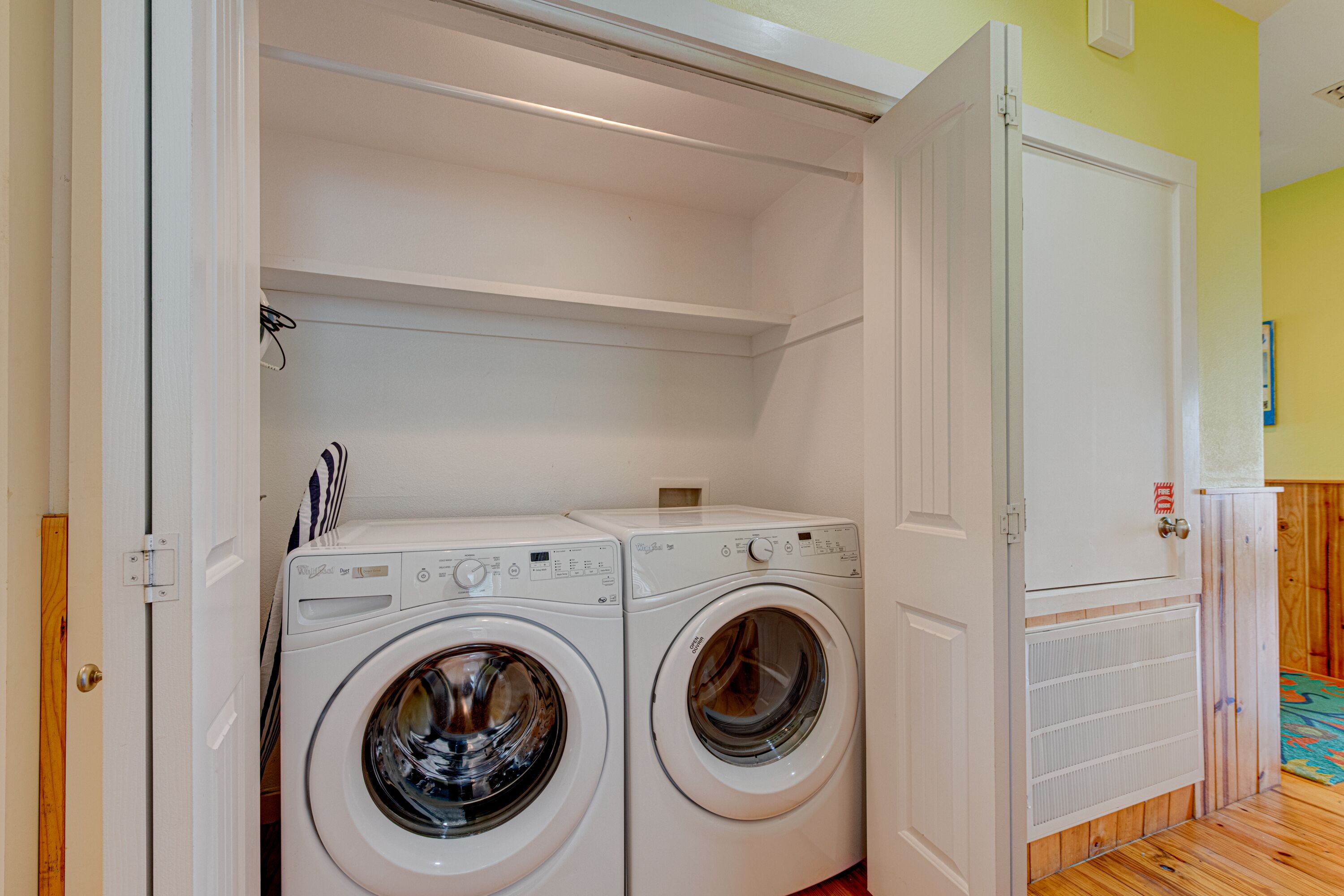 A laundry room with two front-loading washing machines, a white cabinet, and a wooden floor.