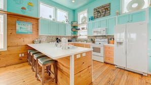 A kitchen with teal cabinets, a white island, wooden stools, and a sign that says "BEACH". - Located in the sought-after gated Village Walk community is a charming tropical (Port Aransas)