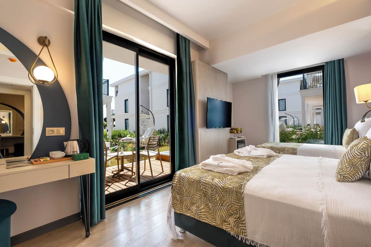 Habitación de hotel con cama, escritorio, televisor y balcón con mobiliario exterior.
