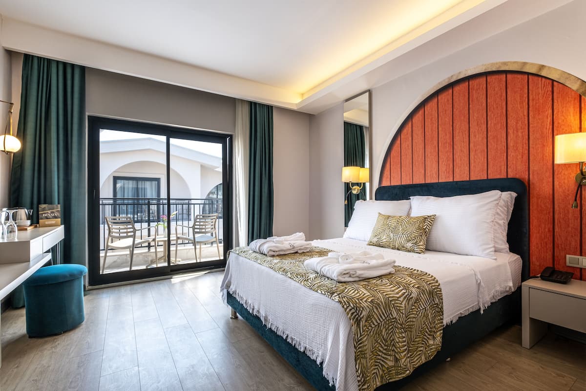Habitación de hotel con cama, escritorio, silla, balcón y un espejo grande.