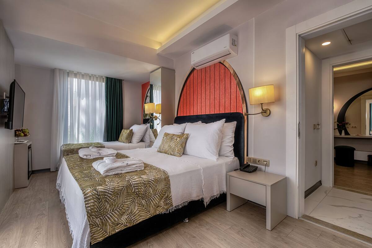 Una habitación de hotel con cama, mesita de noche, lámpara, aire acondicionado y un espejo.