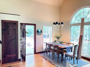 Enjoy meals in this elegant dining area with a wooden table and four chairs, surrounded by a large window and a chandelier.