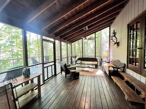 Relax on the covered porch with a sofa, bench, and cushioned seating, surrounded by lush views.