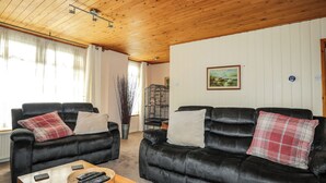 Una sala de estar con dos sofás de cuero negro, una mesa de centro de madera con controles remotos, y un cuadro en la pared.