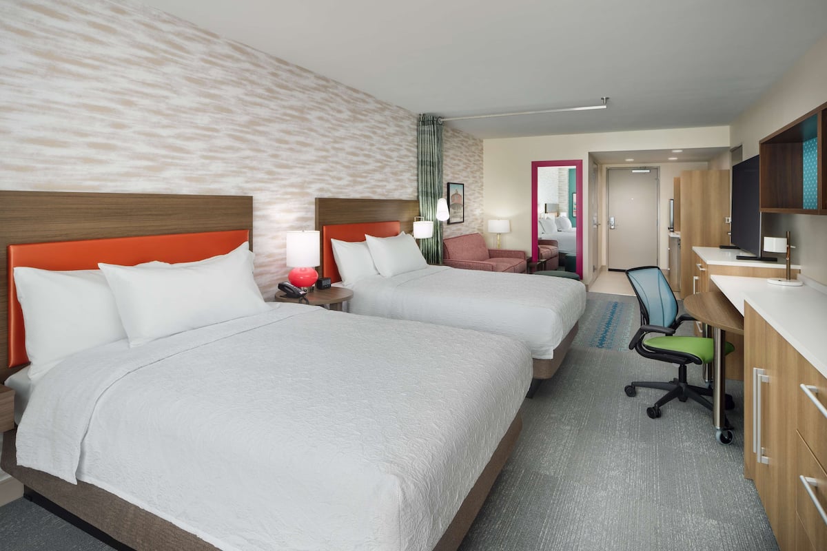 A hotel room with two beds, a desk, a chair, and a TV.
