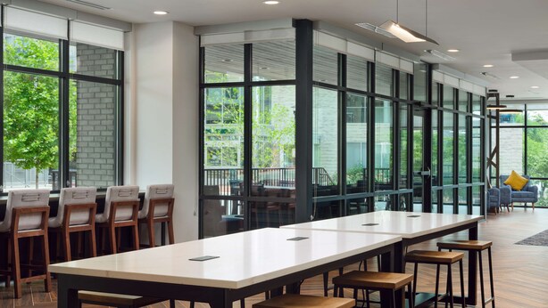 A modern conference room with a long table, multiple chairs, and large windows offering a view of greenery outside. - Home2 Suites by Hilton Towson (Towson)