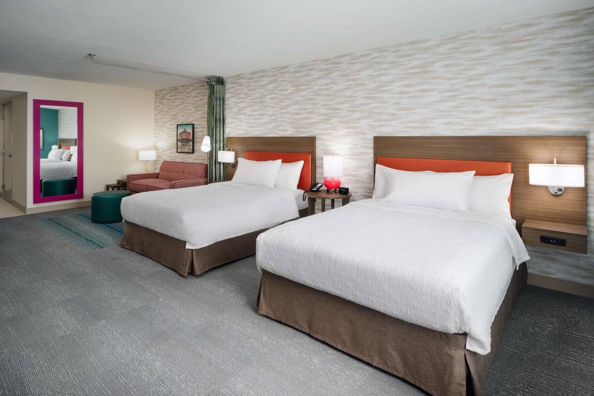 A hotel room with two beds, a sofa, a mirror, and a small table.