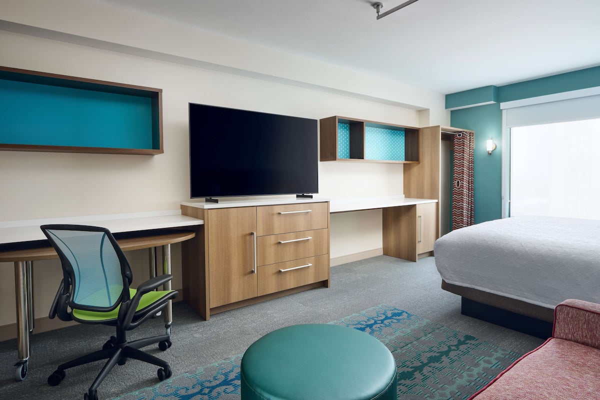 A hotel room with a bed, a desk with a chair, a television, and a wardrobe.