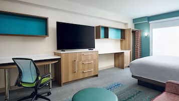 A hotel room with a bed, a desk with a chair, a television, and a wardrobe.