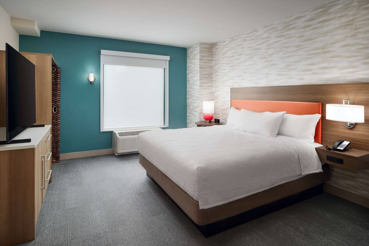 A hotel room with a bed, a television, a desk, and a window.