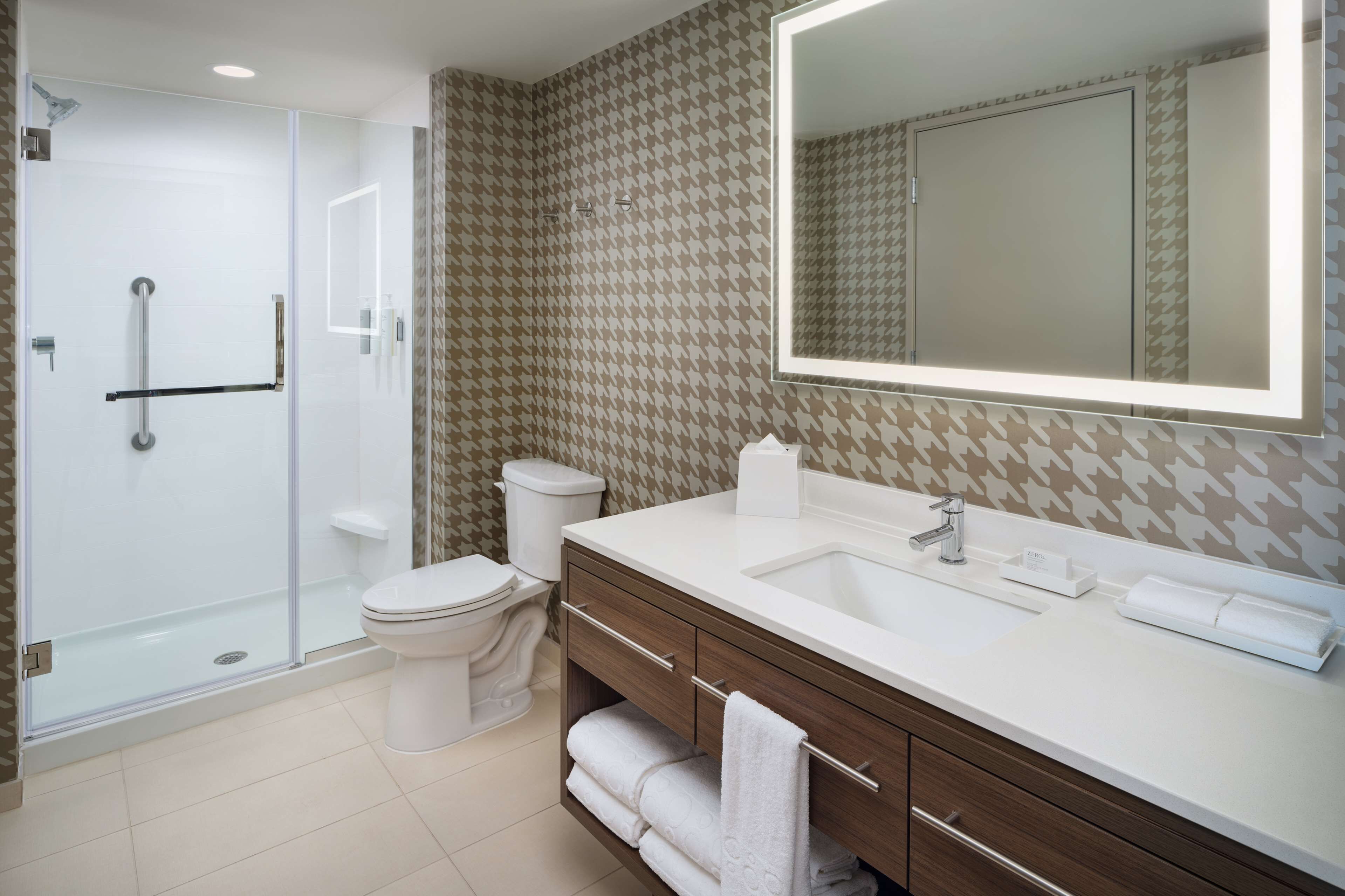 A modern bathroom with a glass-enclosed shower, a white toilet, a large mirror, and a wooden vanity with a sink.