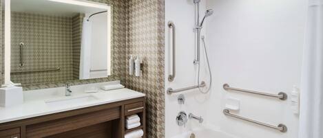 Un baño con un espejo grande, dos lavamanos, una bañera y barras de apoyo.