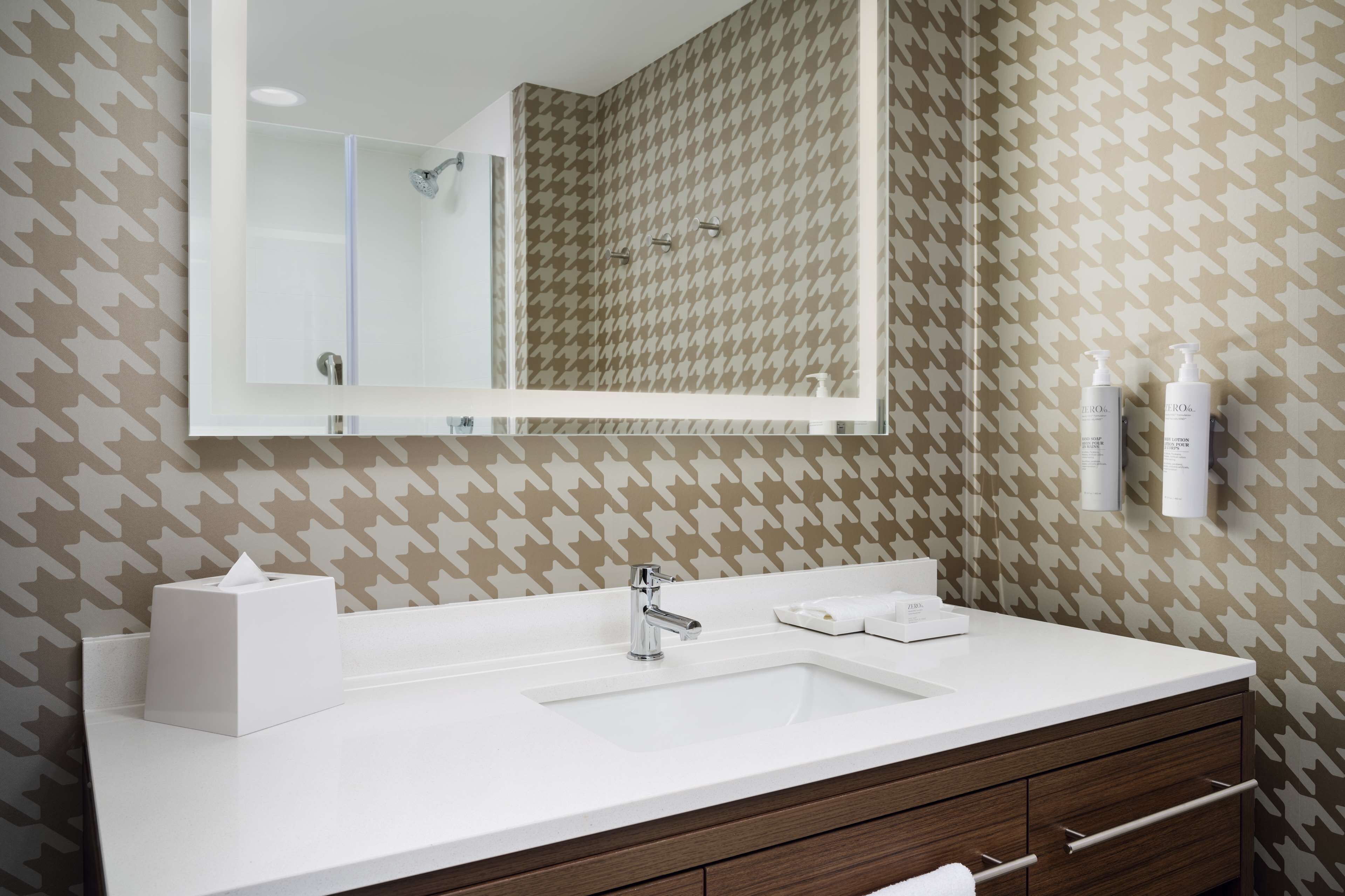 Un baño con lavamanos blanco, un espejo y papel tapiz estampado.