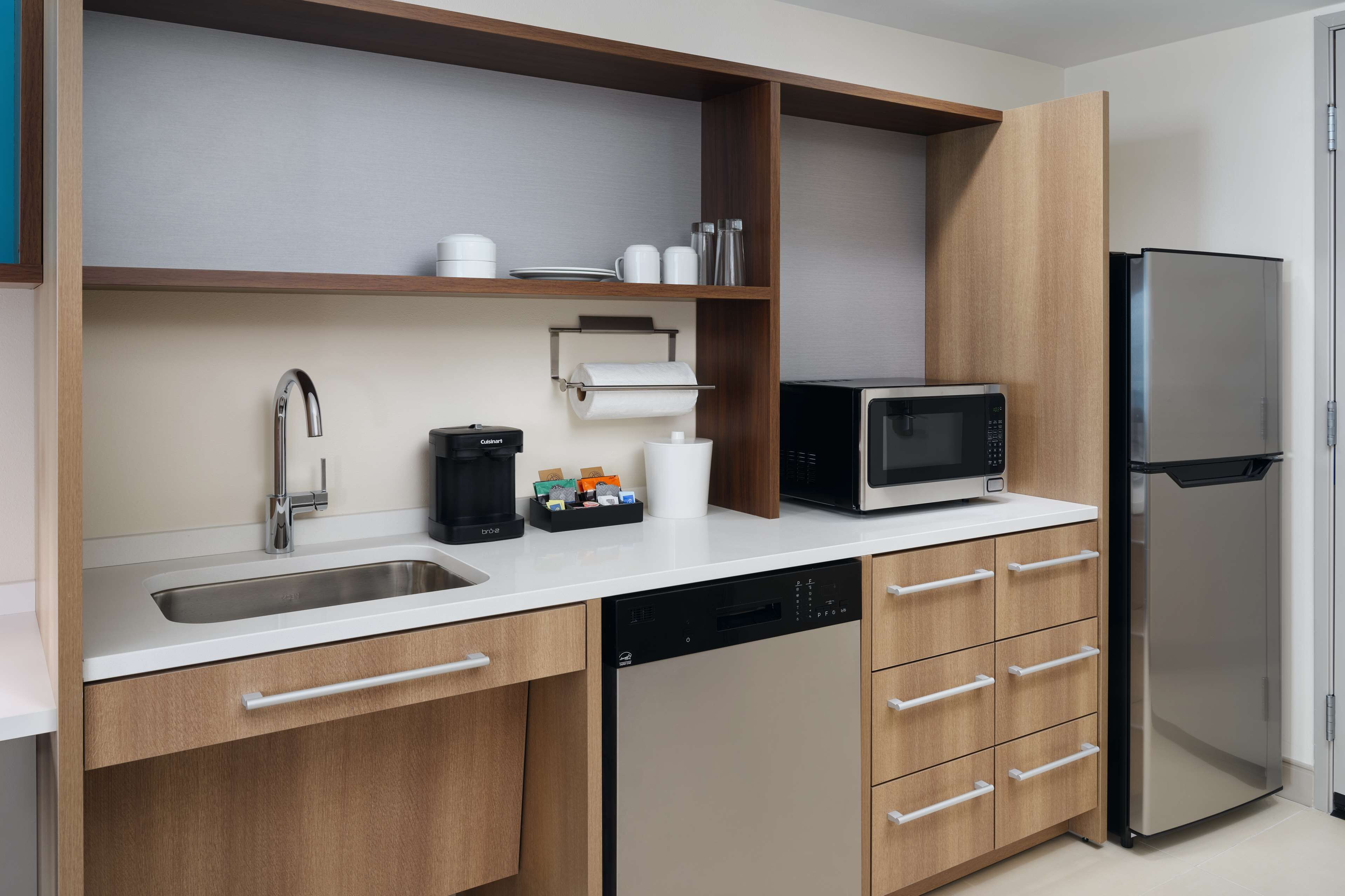 A modern kitchen with a stainless steel sink, a coffee maker, a microwave, and a refrigerator.