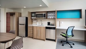A compact kitchen with a microwave, coffee maker, and a dishwasher. There is a dining table with chairs and a small office area with a desk and chair. - Home2 Suites by Hilton Towson (Towson)