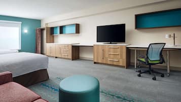 Quarto de hotel com cama, escrivaninha, cadeira, televisão e janela.