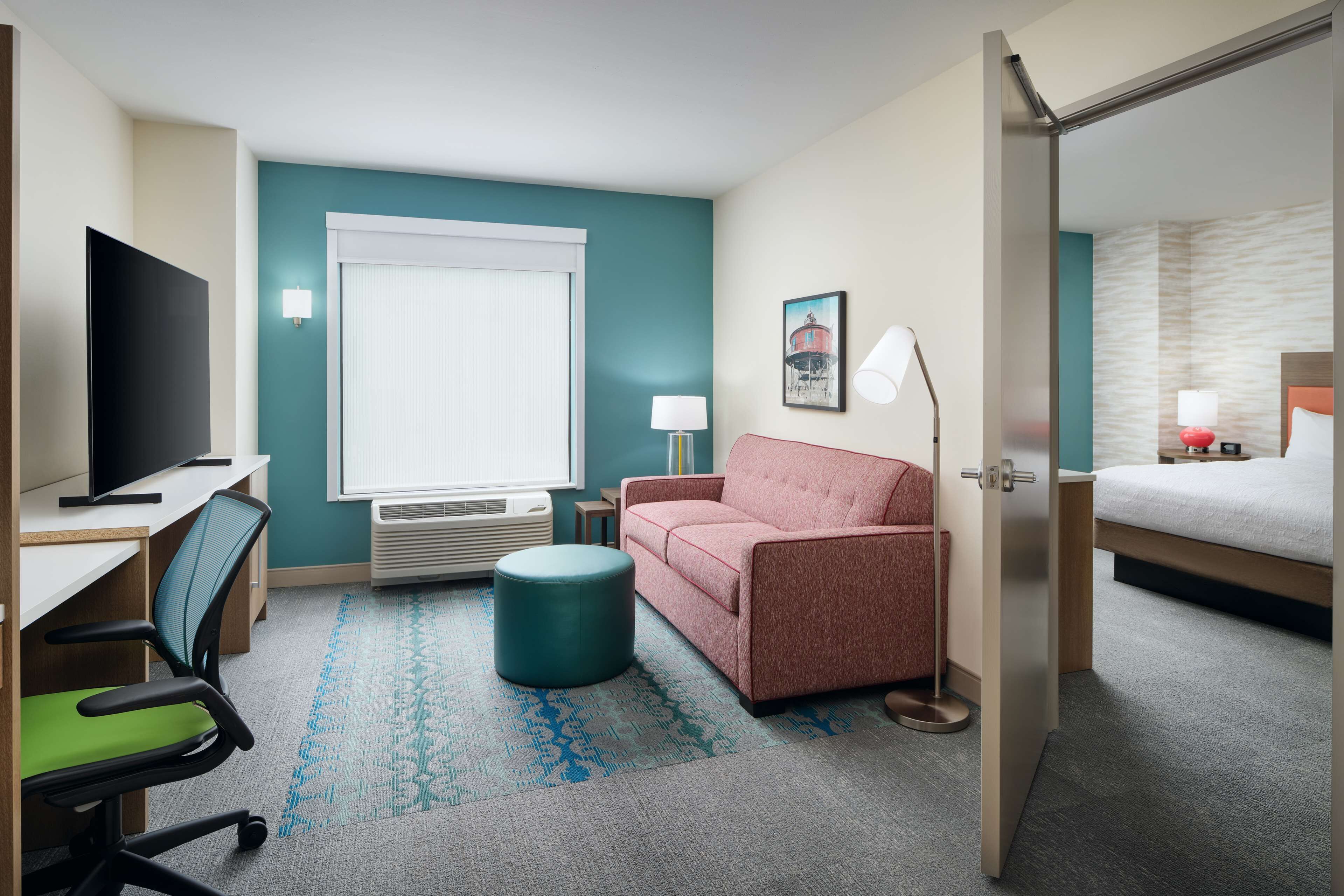 Habitación de hotel con cama, escritorio con silla, sofá, lámpara y televisor.