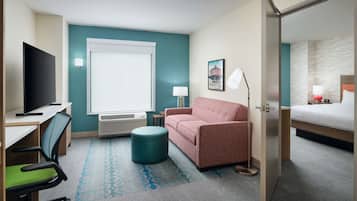 Habitación de hotel con cama, escritorio con silla, sofá, lámpara y televisor.