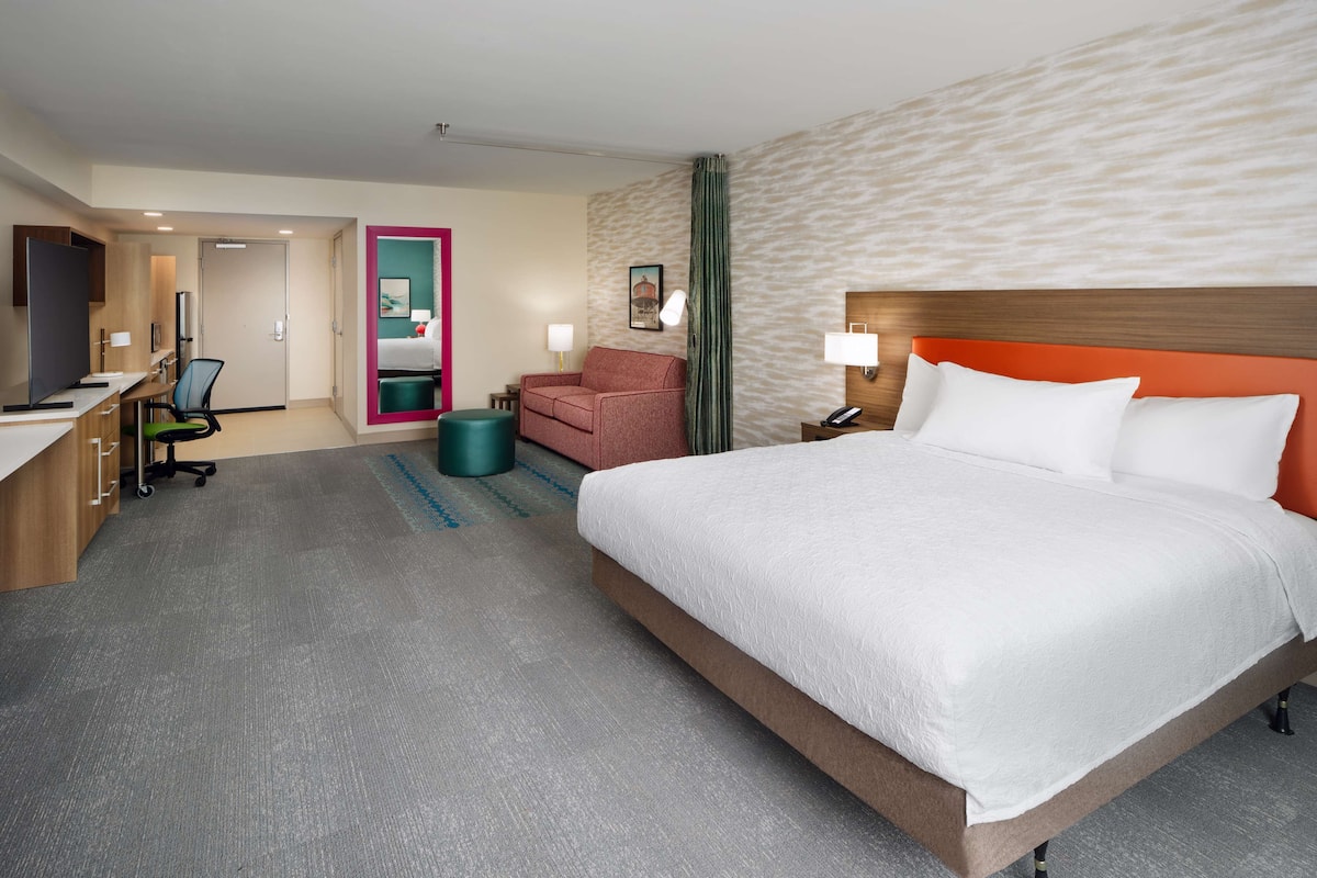 A hotel room with a bed, desk, chair, and a small seating area.