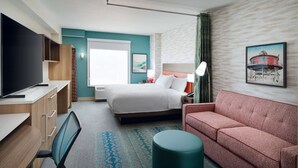 A hotel room with a bed, a sofa, a desk with a TV, and a chair. - Home2 Suites by Hilton Towson (Towson)